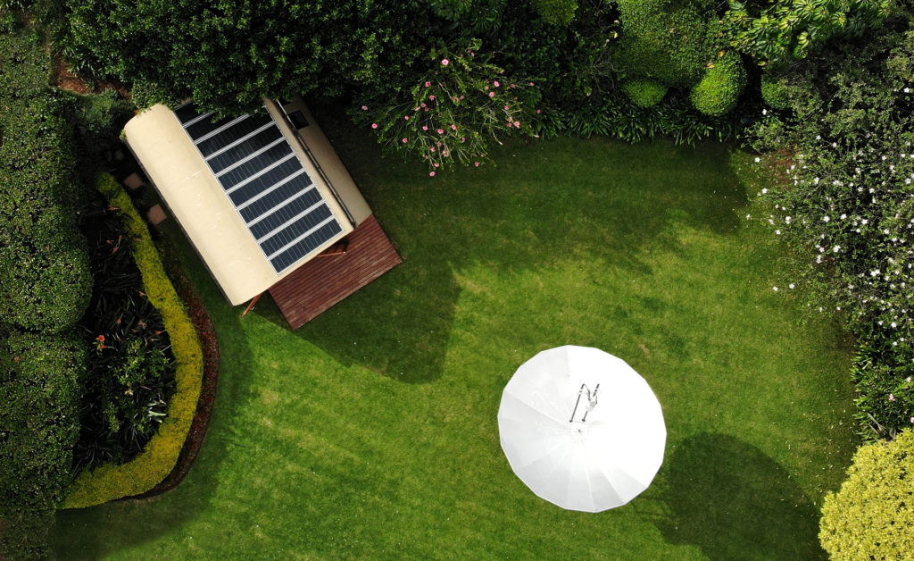 Aerial view of a lush garden with green grass and bordering bushes, featuring the Ambassador's cottage in the top left corner.